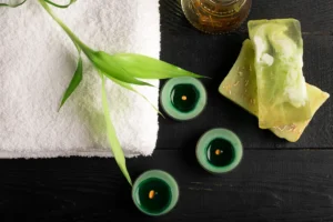 Deep tissue massage setup with white towel, herbal oil, handmade soap bars, green candles, and bamboo.