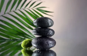 Hot stone massage concept with stacked wet basalt stones and tropical leaf.